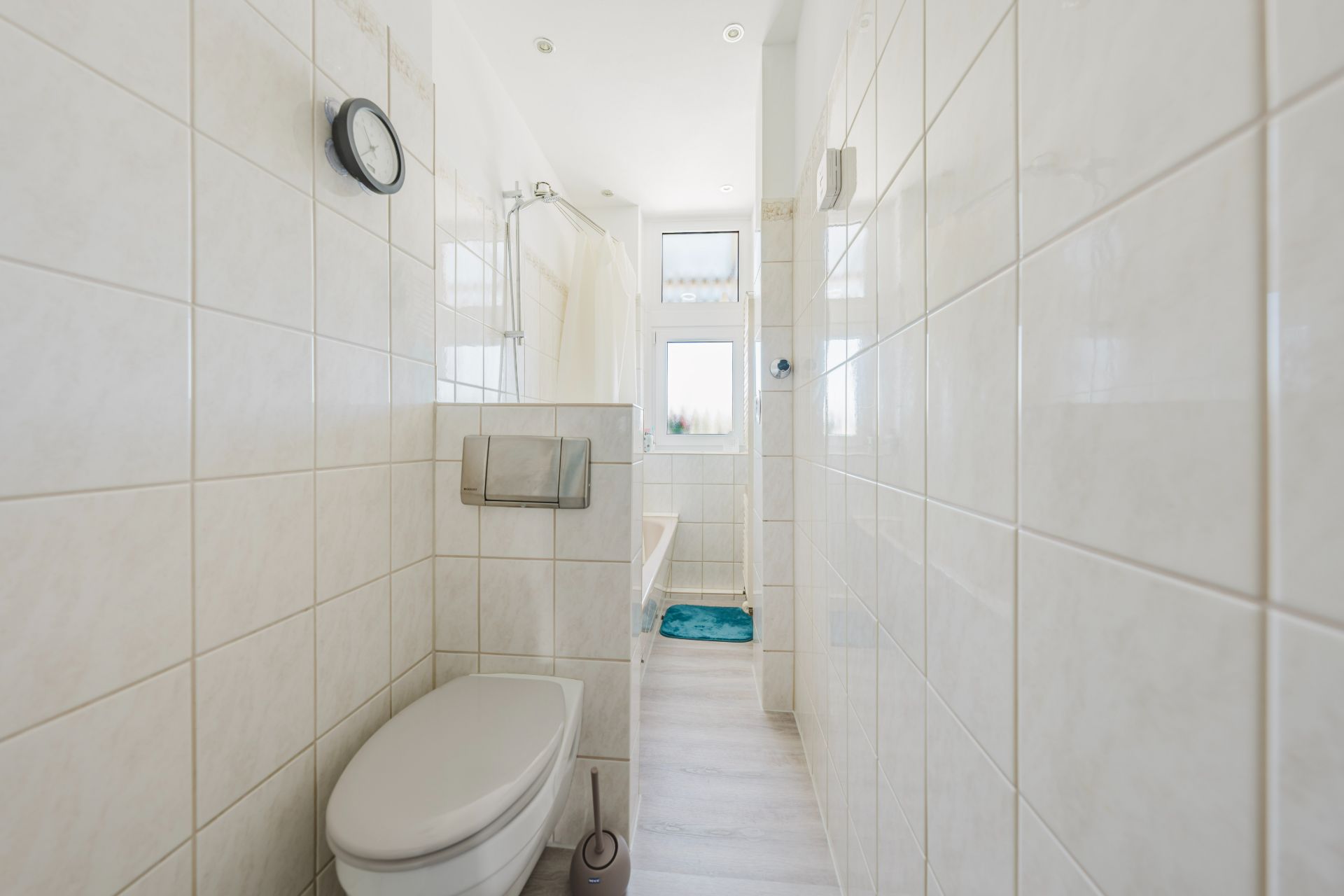 Helles Badezimmer mit WC, Badewanne, Fenster und hellen Fliesen.