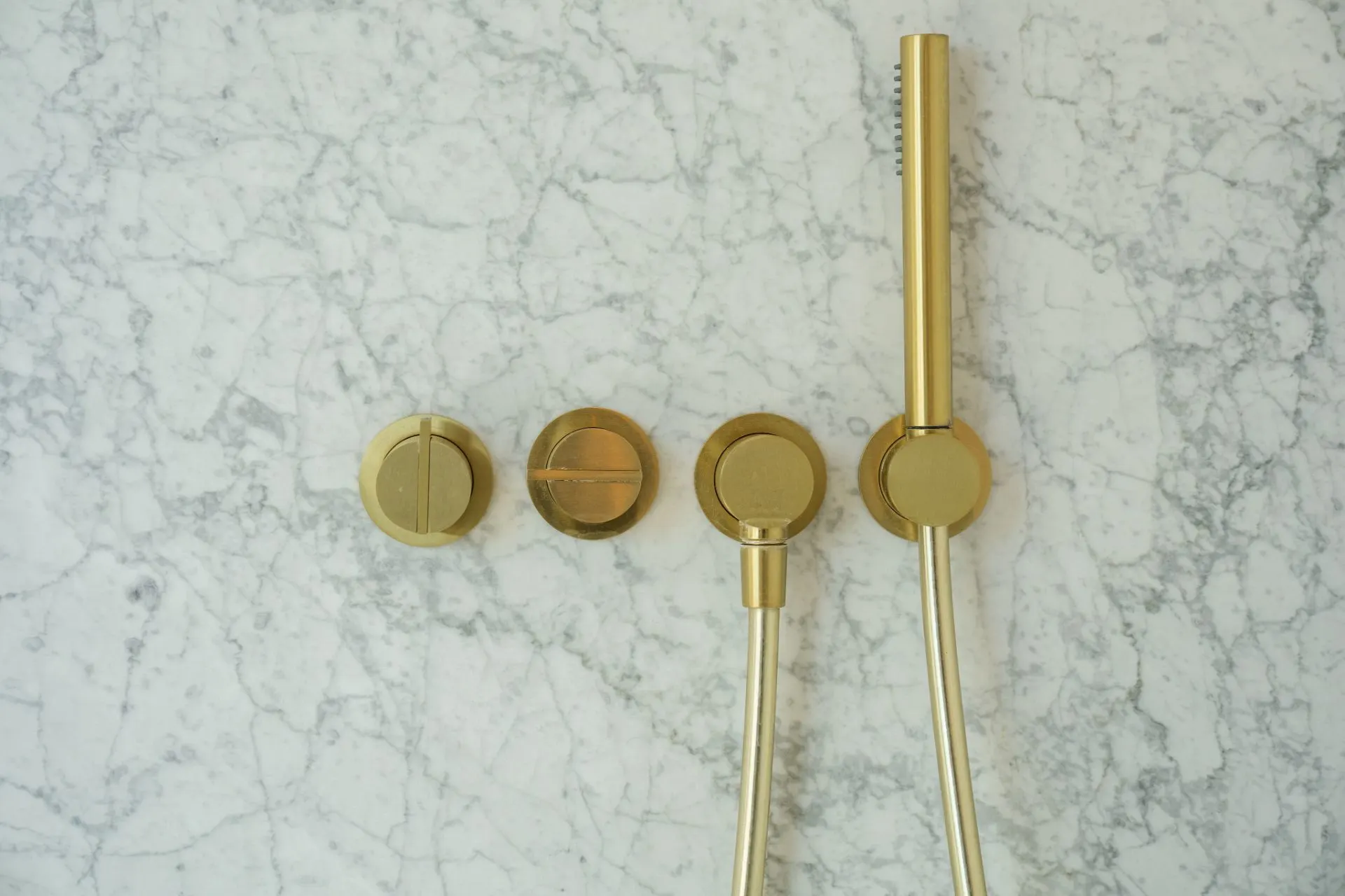 Goldene Armaturen und Handbrause auf heller Marmorwand.