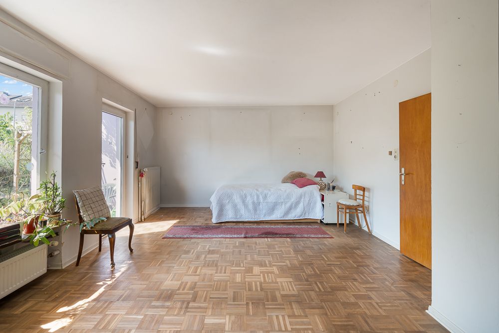 Helles Schlafzimmer mit Bett, Holzboden, Fenster, Tür und wenigen Möbeln.