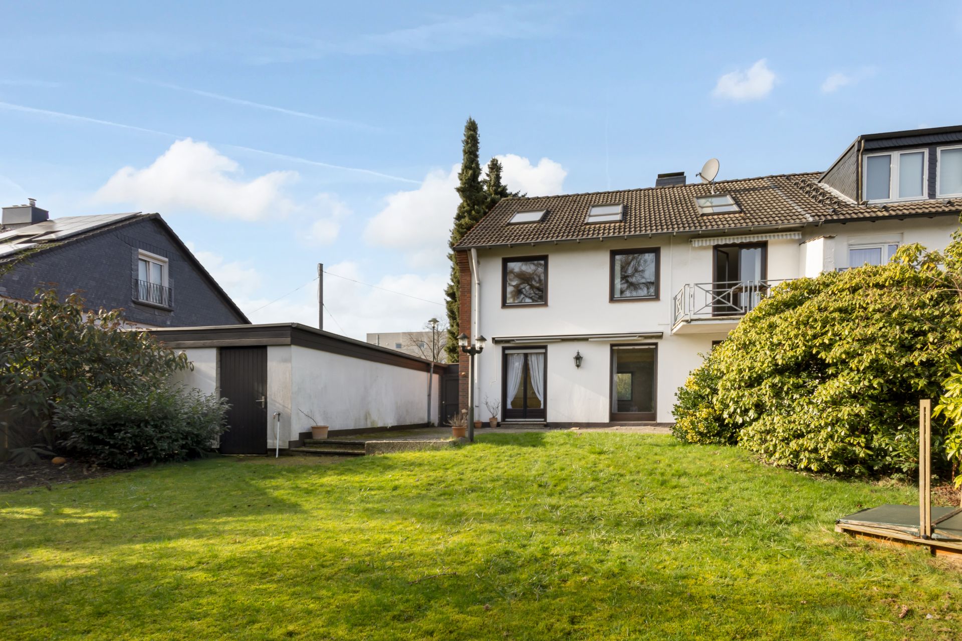 Zweistöckiges Wohnhaus mit Garten, Terrasse und angrenzender Garage an einem sonnigen Tag.