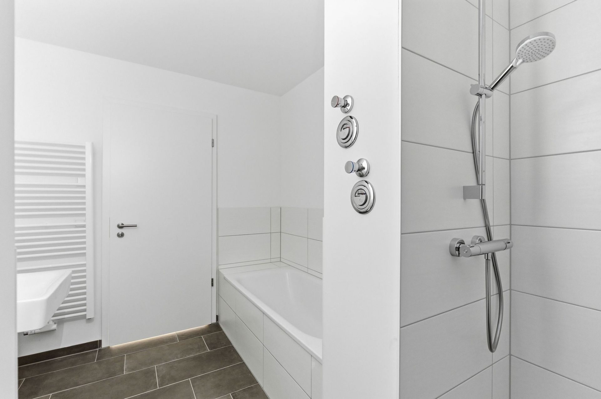 Modernes Bad mit Dusche, Badewanne, Waschbecken und weißem Handtuchheizkörper.
