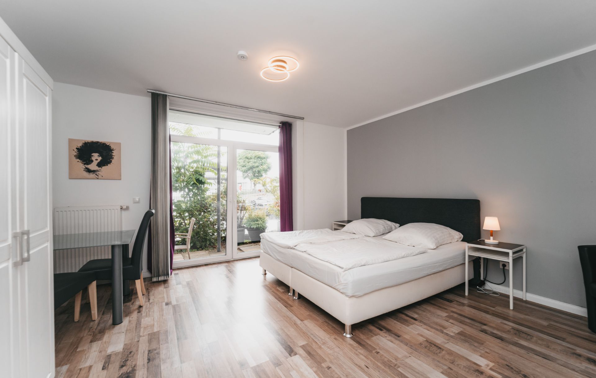Helles Schlafzimmer mit Doppelbett, Nachttisch, Schreibtisch und Zugang zu einer Terrasse mit Gartenblick.