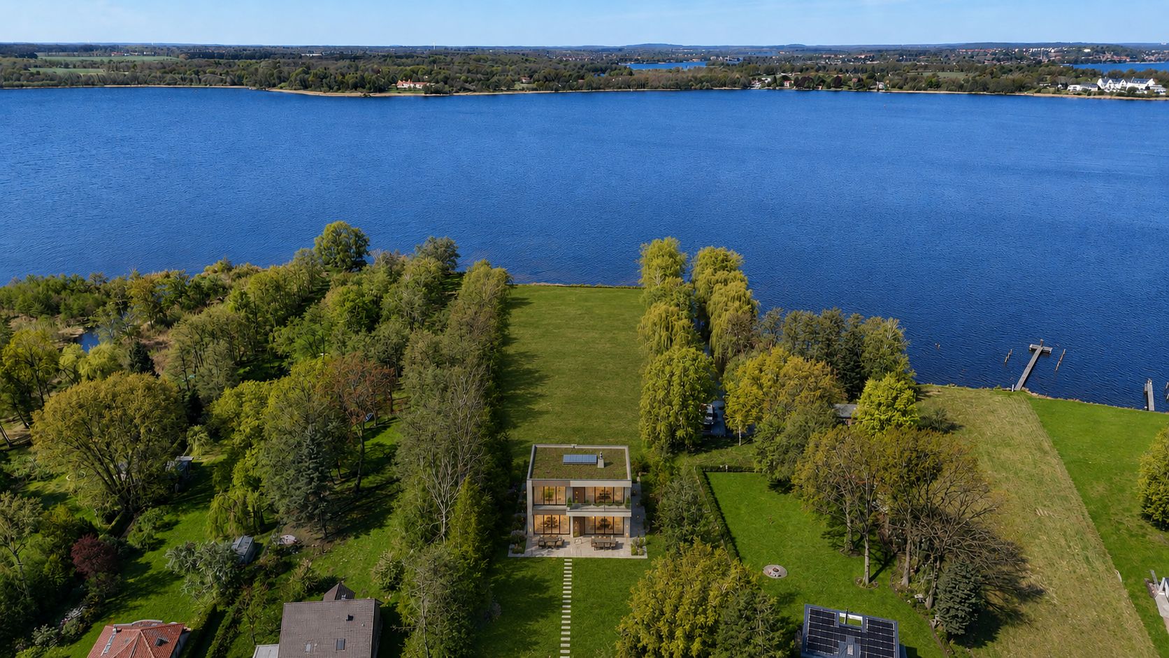 Luftbild eines modernen Hauses mit großem Garten direkt am Seeufer.