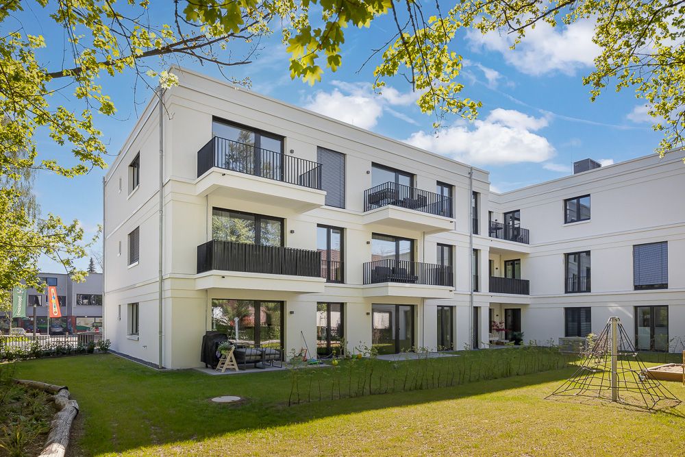 Modernes, dreistöckiges Wohngebäude mit Balkonen und Gartenbereich im Vordergrund.