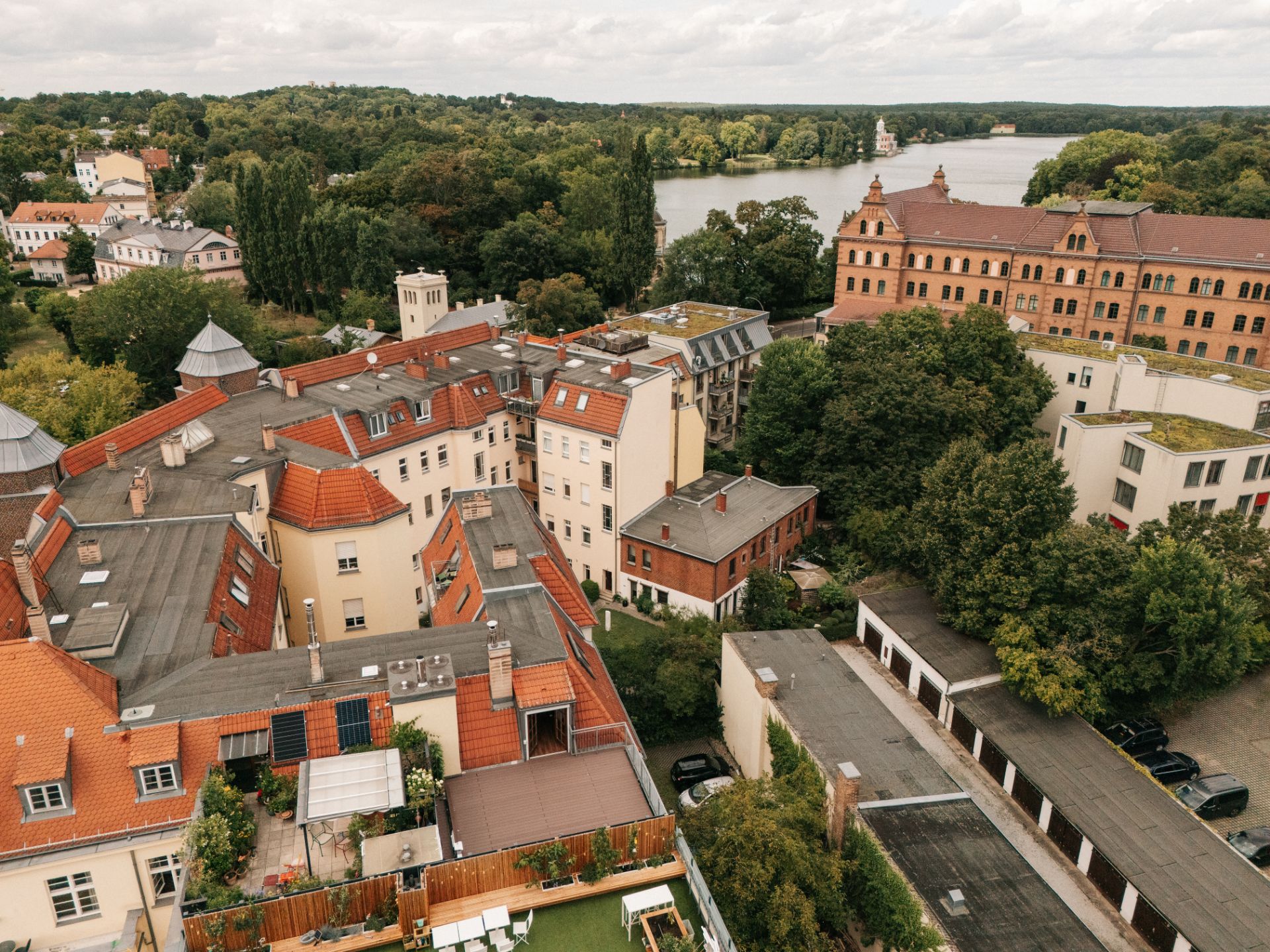 Luftaufnahme von Wohnhäusern mit roten Dächern, viel Grün und einem See im Hintergrund.
