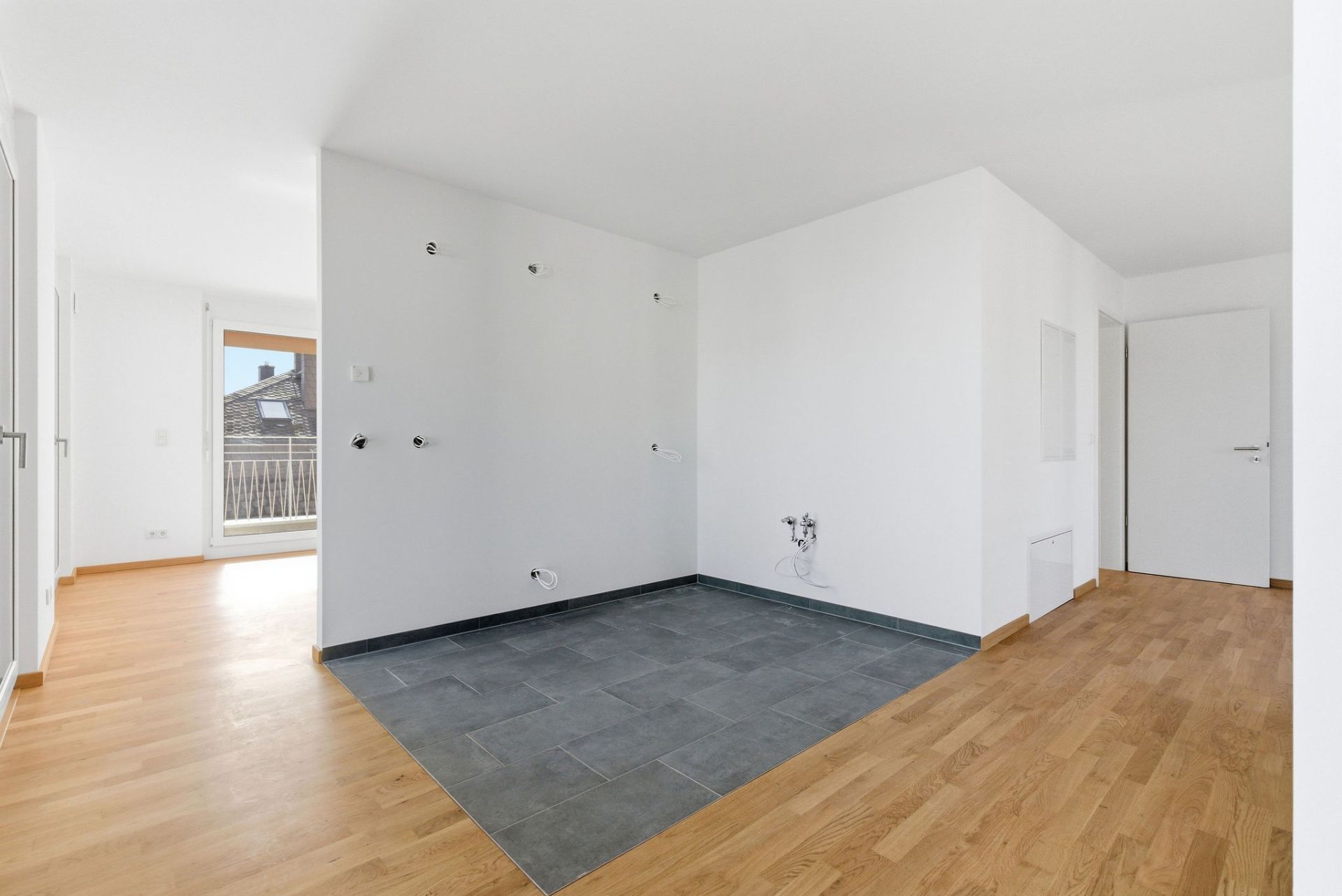 Helle, leere Wohnung mit Parkettboden und abgetrenntem Bereich mit dunklen Fliesen.