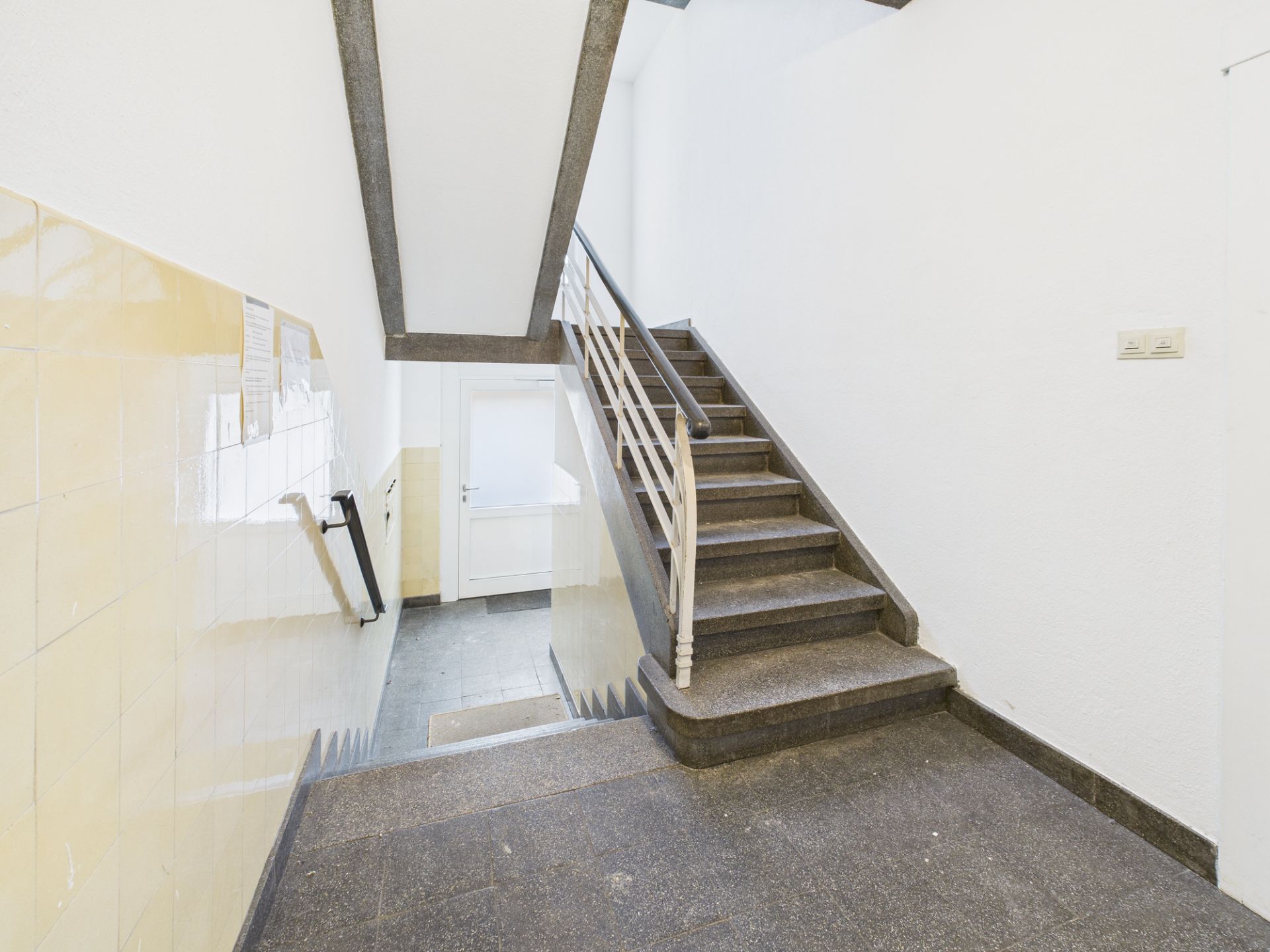Staircase in einem Wohnhaus mit gelben Wandfliesen und Handlauf, Tür im Hintergrund.