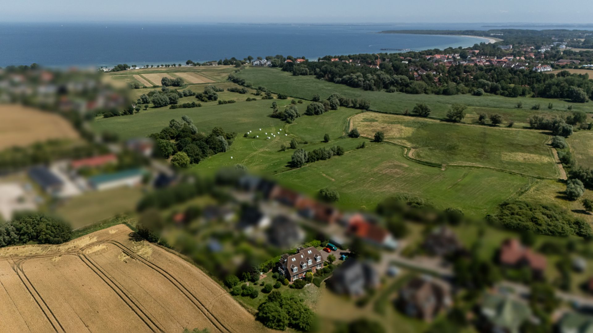 Luftaufnahme eines Wohnhauses mit umliegenden Feldern und Küste im Hintergrund.
