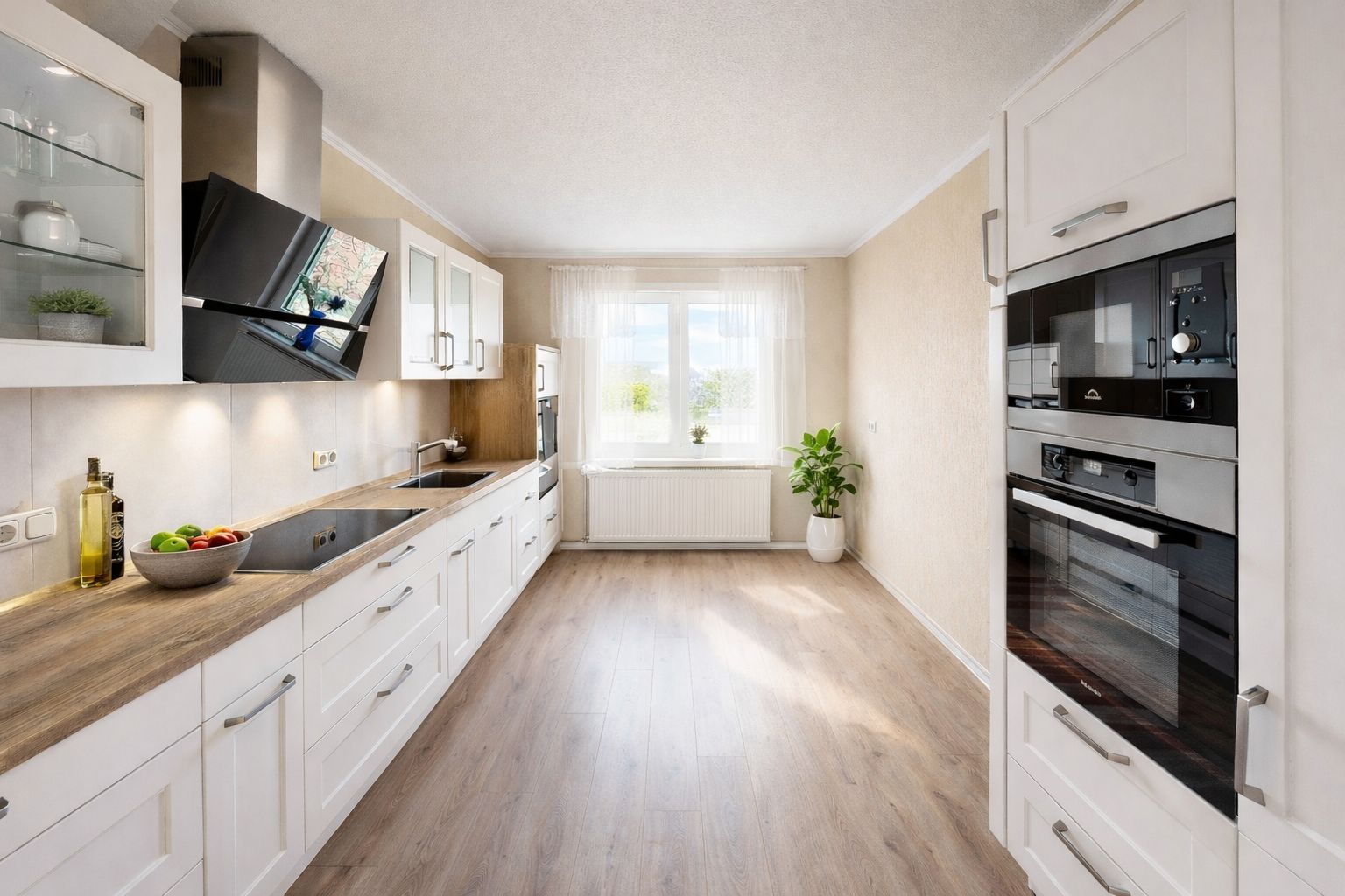 Helle, moderne Küche mit weißen Schränken, Holzboden und großem Fenster.