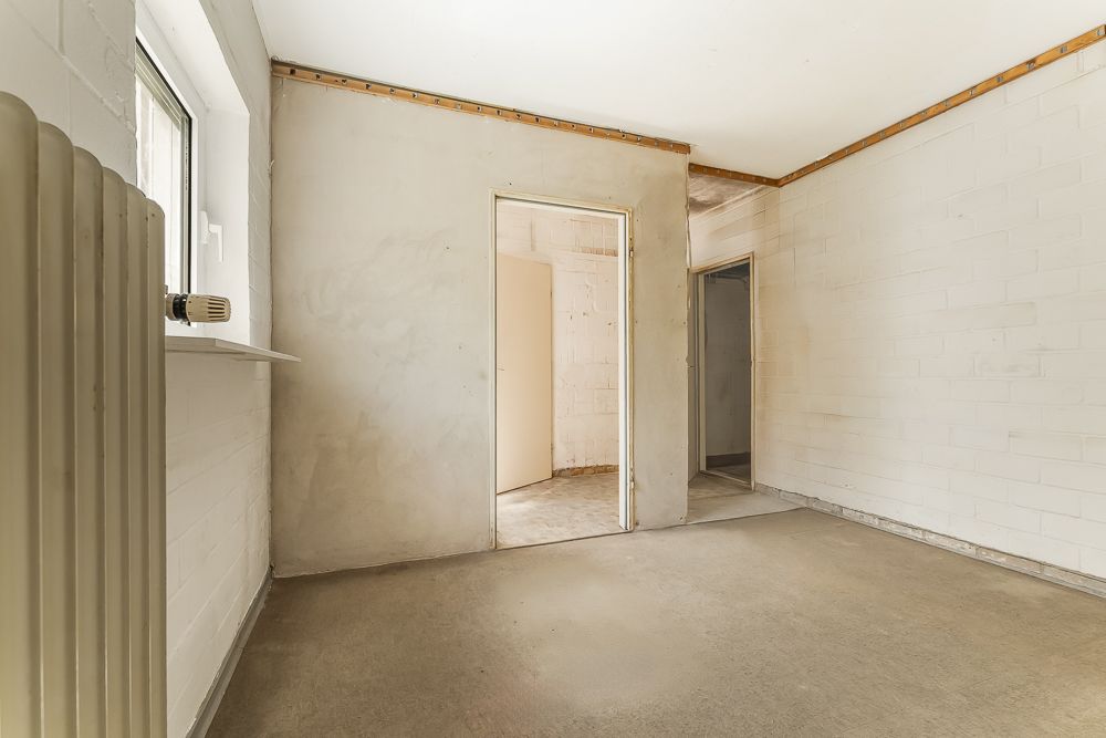Leerer Raum mit beigem Boden, zwei offenen Türen und einem Fenster mit Heizkörper.