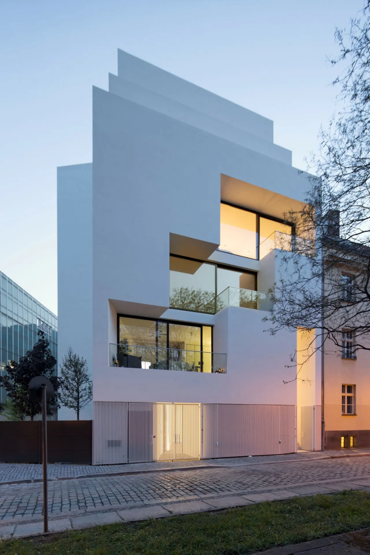 Modernes weißes Wohnhaus mit großen Fenstern und mehreren Terrassen am Abend.