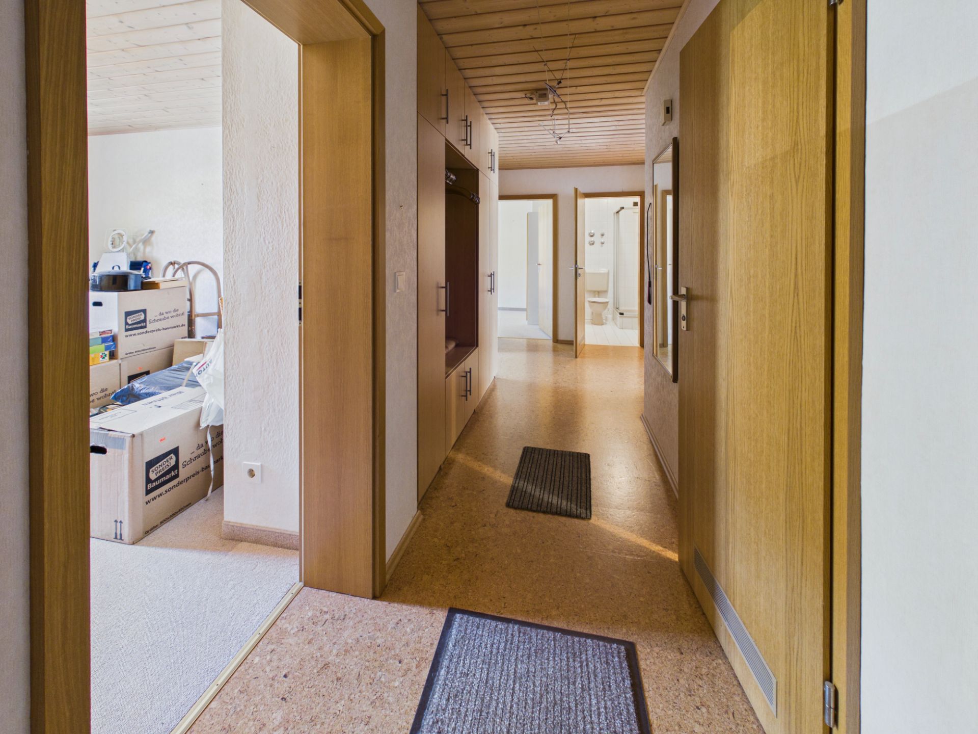 Heller Flur mit Holzboden, mehreren Türen und Blick in ein Zimmer mit Umzugskartons.