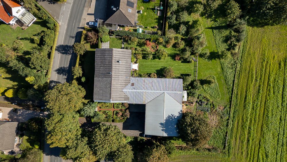 Luftaufnahme eines Hauses mit großem Garten, von Bäumen und einer Straße umgeben.