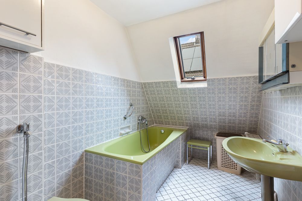 Badezimmer mit grüner Badewanne, grünem Waschbecken und Dachfenster.