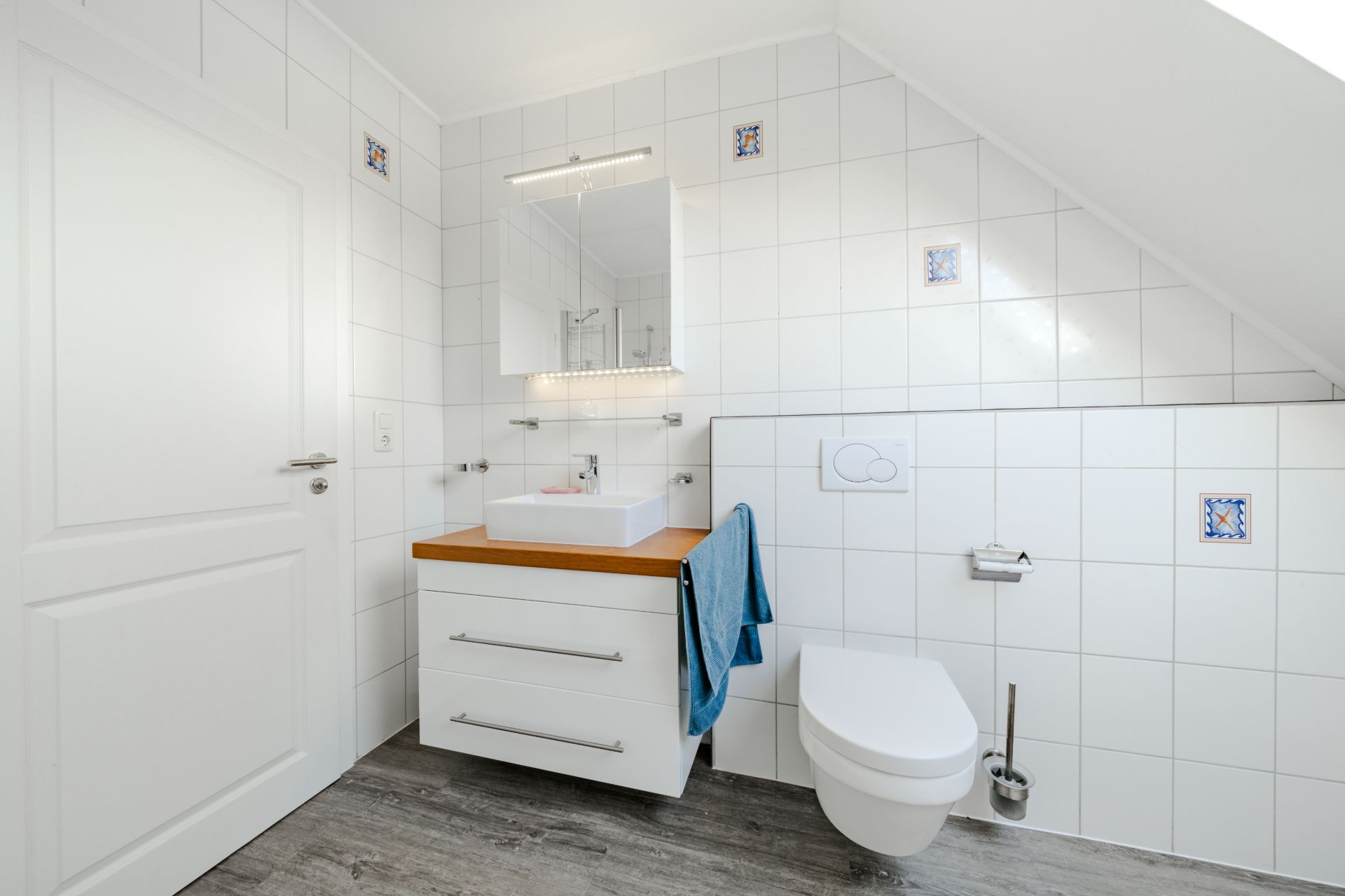 Helles Badezimmer mit Waschbecken, Spiegel, Wand-WC und Handtuch auf einer weißen Kommode.