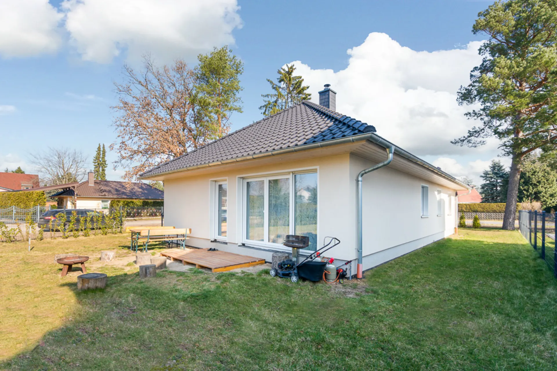 Einfamilienhaus mit Gartenterrasse, Gartenbank, Grill und umliegender Rasenfläche.