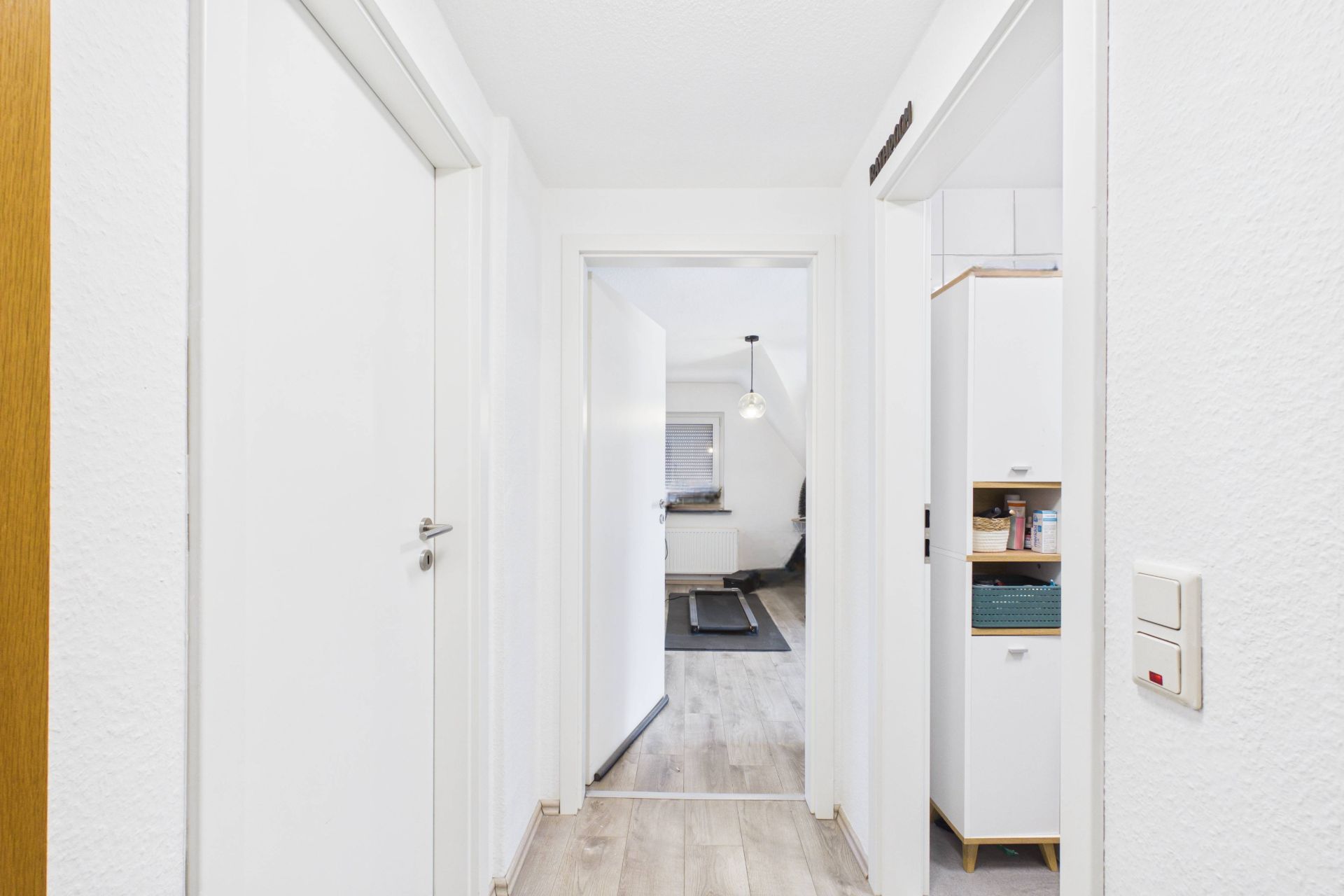 Heller Flur mit weißen Türen und Blick in ein Wohnzimmer mit Holzfußboden.