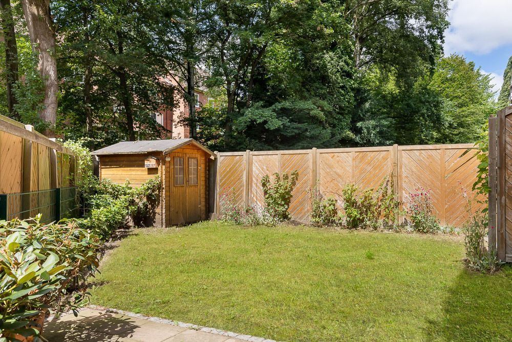 Garten mit Rasenfläche, Holzzaun und kleinem Holzhaus am Rand.