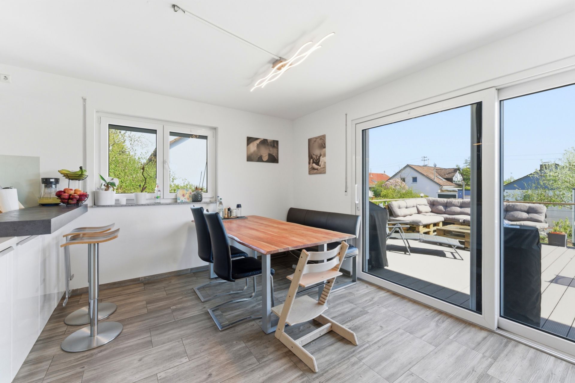 Helles Esszimmer mit Holztisch, Stühlen und Zugang zur Terrasse mit Sitzmöbeln.