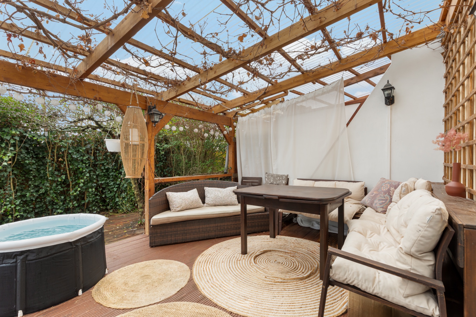 Überdachte Terrasse mit Sitzbereich, Holzmöbeln, Teppichen und kleinem Pool.