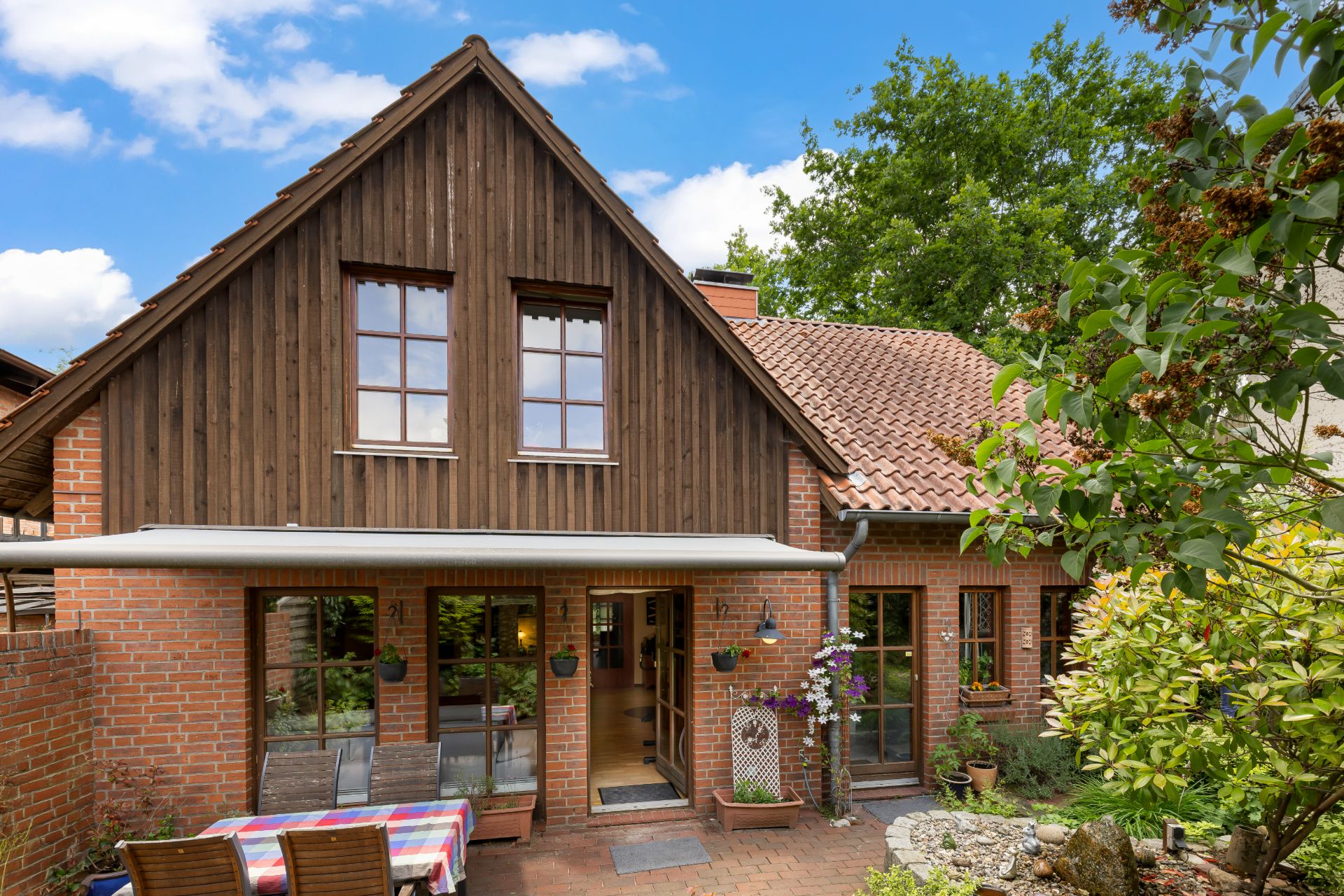 Backsteinwohnhaus mit Holzgiebelfassade und Terrasse mit Tisch und Stühlen im Garten.