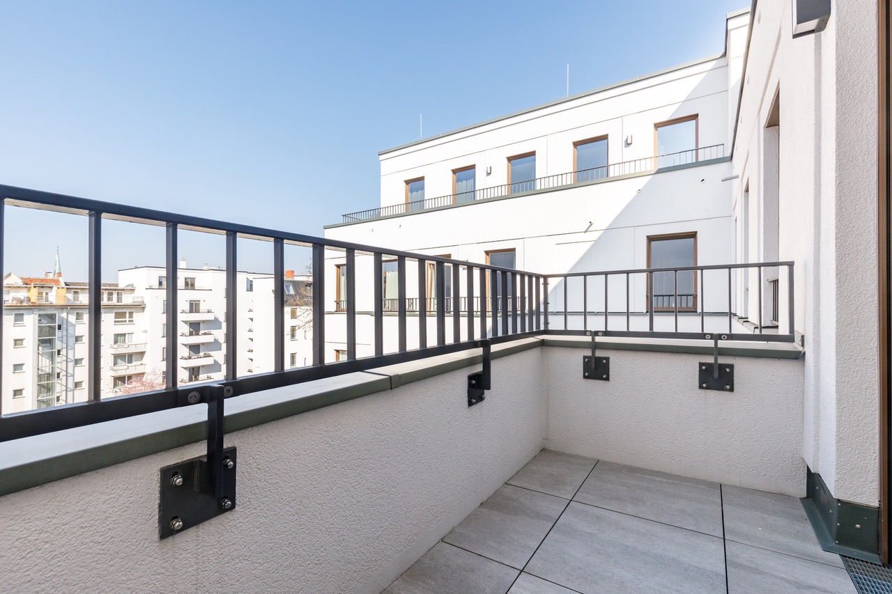Balkon mit Fliesenboden und Metallgeländer, Blick auf benachbarte Wohngebäude.