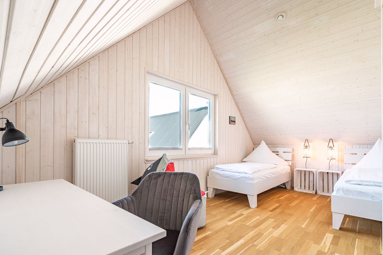 Helles Schlafzimmer mit zwei Einzelbetten, Schreibtisch und Stuhl unter Dachschräge.
