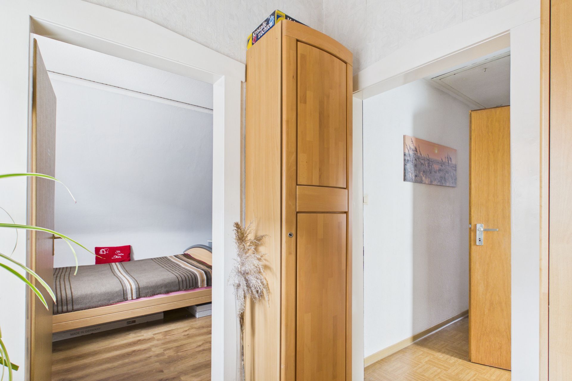 Flur mit Holzschrank, Blick in ein Schlafzimmer mit Bett und offene Tür zu einem weiteren Raum.
