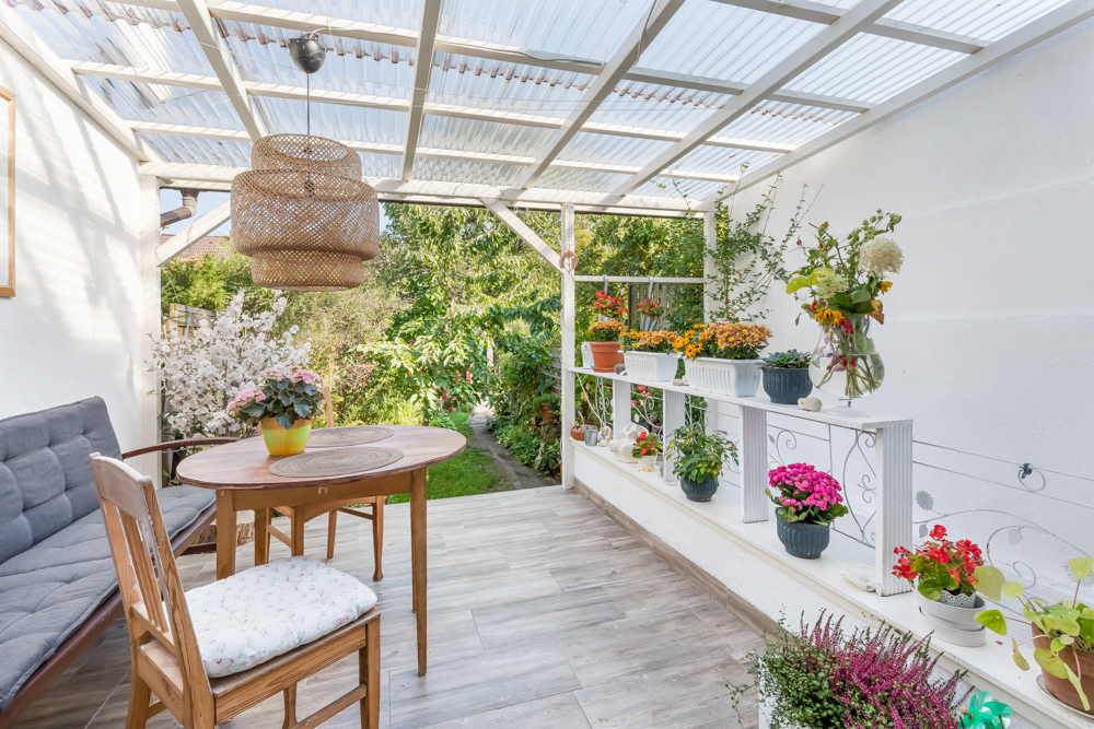 Überdachte Terrasse mit Holztisch, Stuhl, Sitzbank und vielen Blumentöpfen.