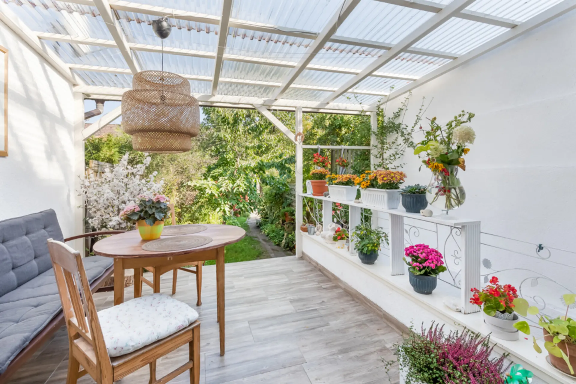 Überdachte Terrasse mit Holztisch, Stuhl, Sitzbank und vielen Blumentöpfen.