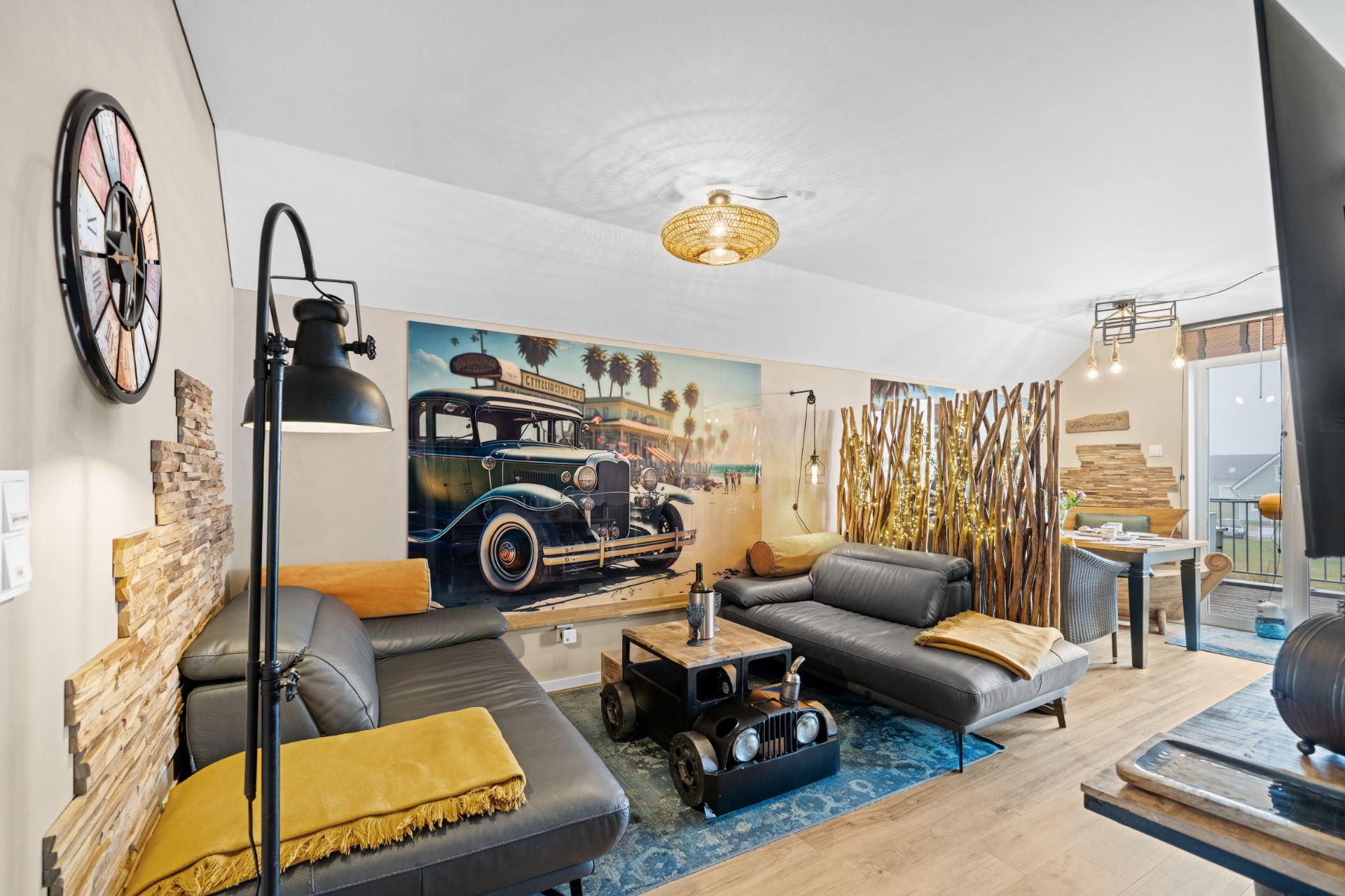 Modernes Wohnzimmer mit zwei grauen Sofas, großem Wandbild eines Oldtimers und Holztisch.