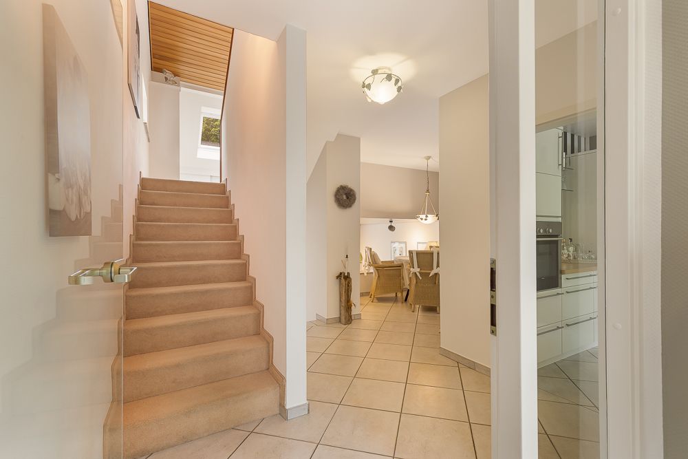 Heller Flur mit Treppe, Blick ins Esszimmer und teilweise sichtbarer Küche.