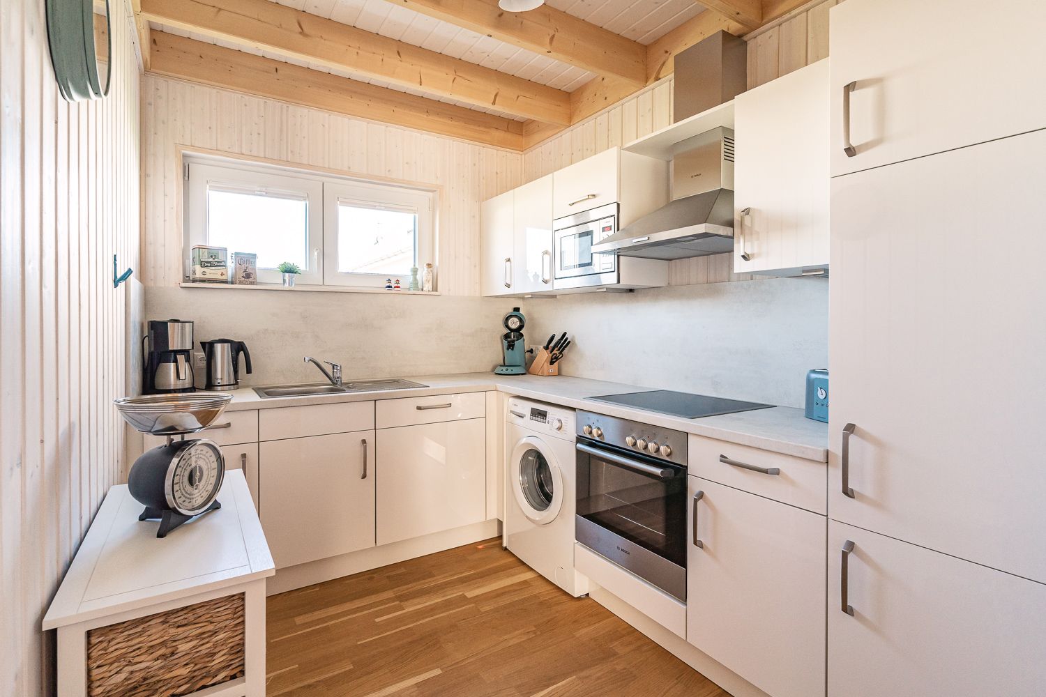 Helle, moderne Küche mit weißen Schränken, Holzdecke und Haushaltsgeräten.
