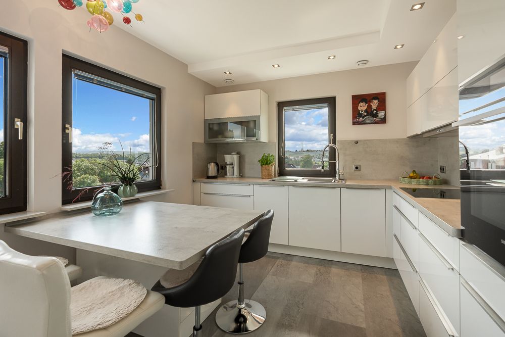 Moderne Küche mit weißen Schränken, Esstisch, drei Stühlen und großen Fenstern mit Ausblick.