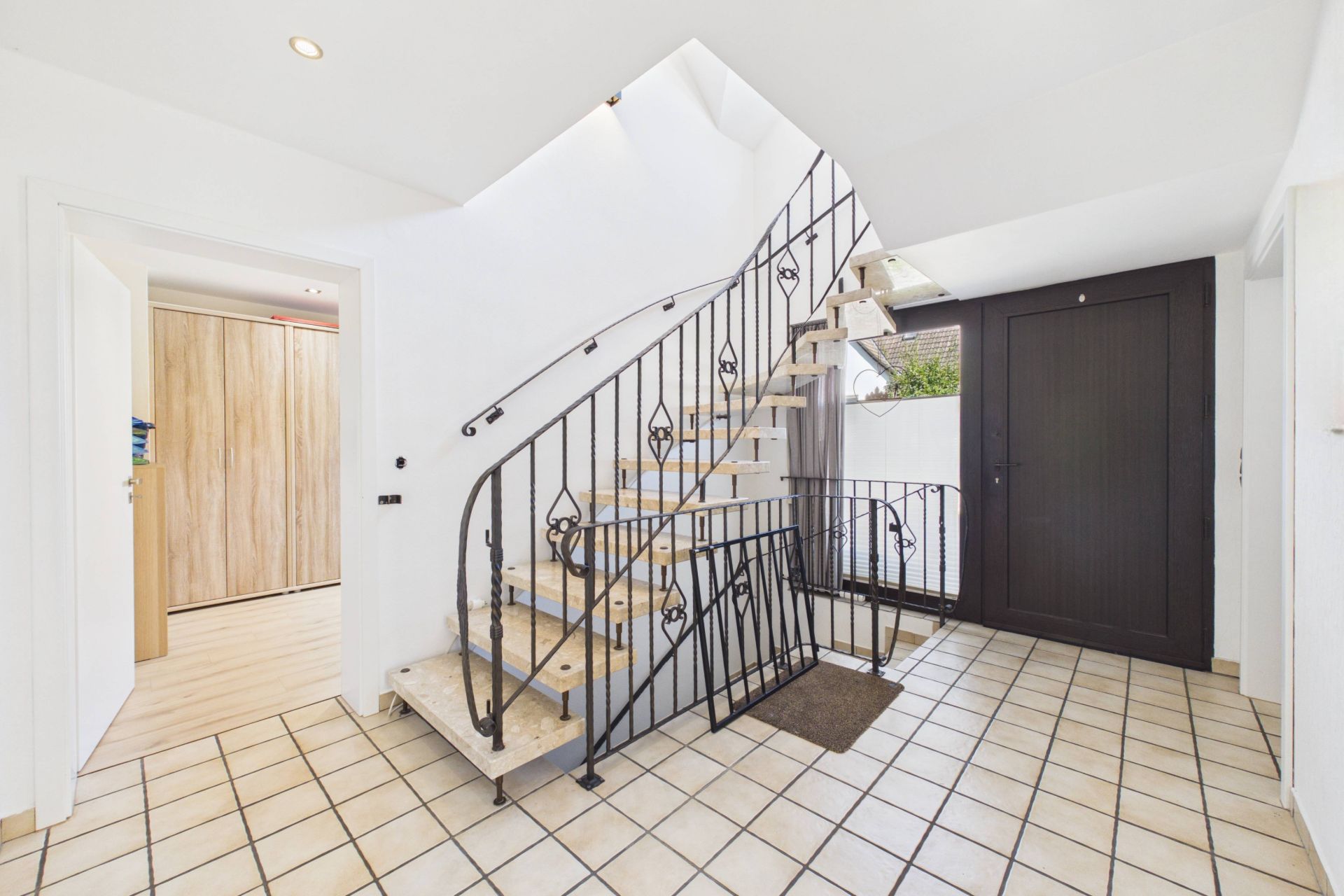 Heller Flur mit Fliesenboden und offener Treppe mit schwarzem Geländer.