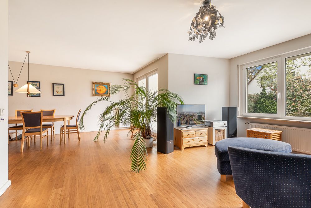 Helles Wohnzimmer mit Holzfußboden, Essbereich, großen Fenstern, Pflanze und Sesseln.