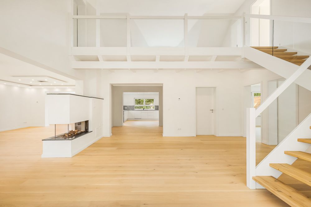 Helles Wohnzimmer mit Kamin, Holztreppe und offener Galerie, Blick in die Küche.