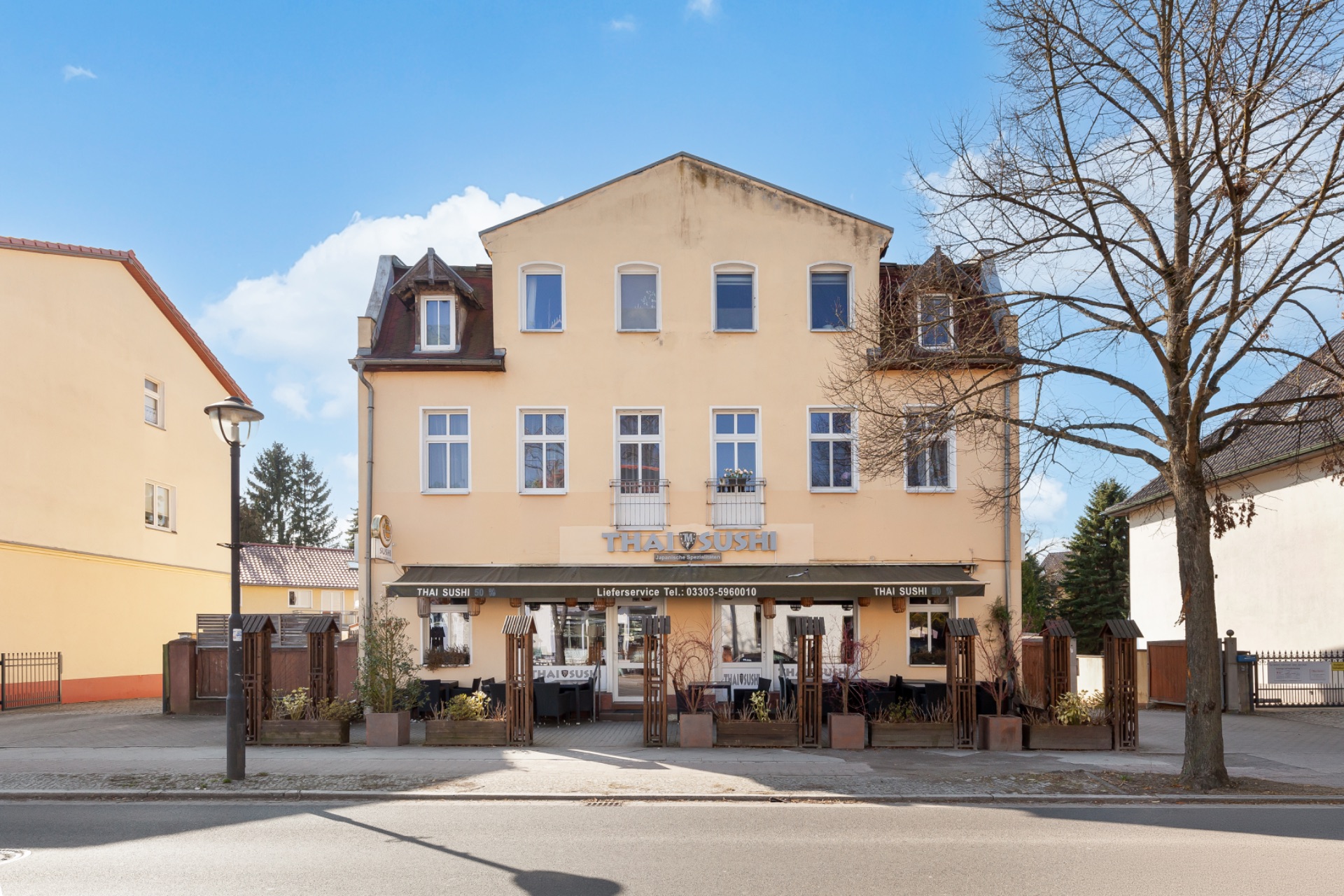 Dreistöckiges Wohnhaus mit Außenbereich und Bäumen, Blick von der Straße.