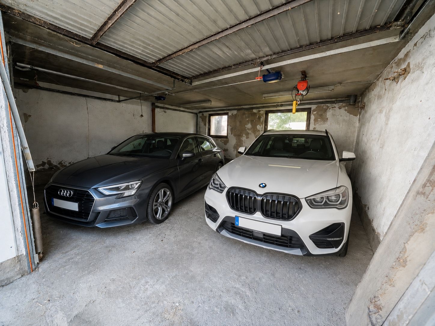 Zwei Autos stehen nebeneinander in einer einfachen Doppelgarage mit Betonboden.