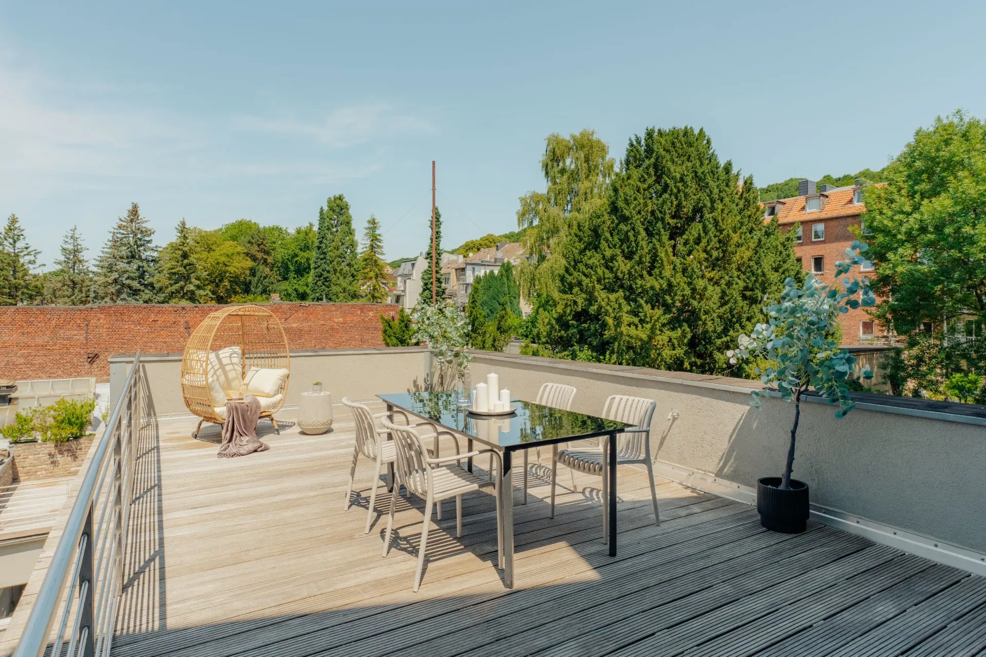 Große Dachterrasse mit Esstisch, Stühlen, Lounge-Sessel und Pflanzen, umgeben von Bäumen.