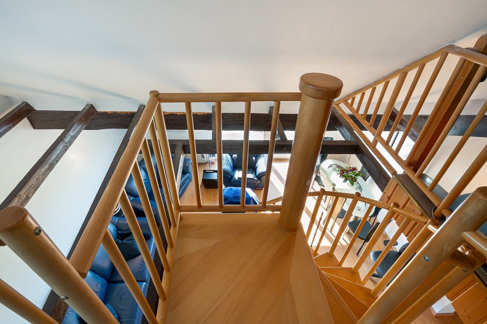 Holztreppe mit Geländer, Blick von oben auf ein Wohnzimmer mit blauen Sofas und Tisch.
