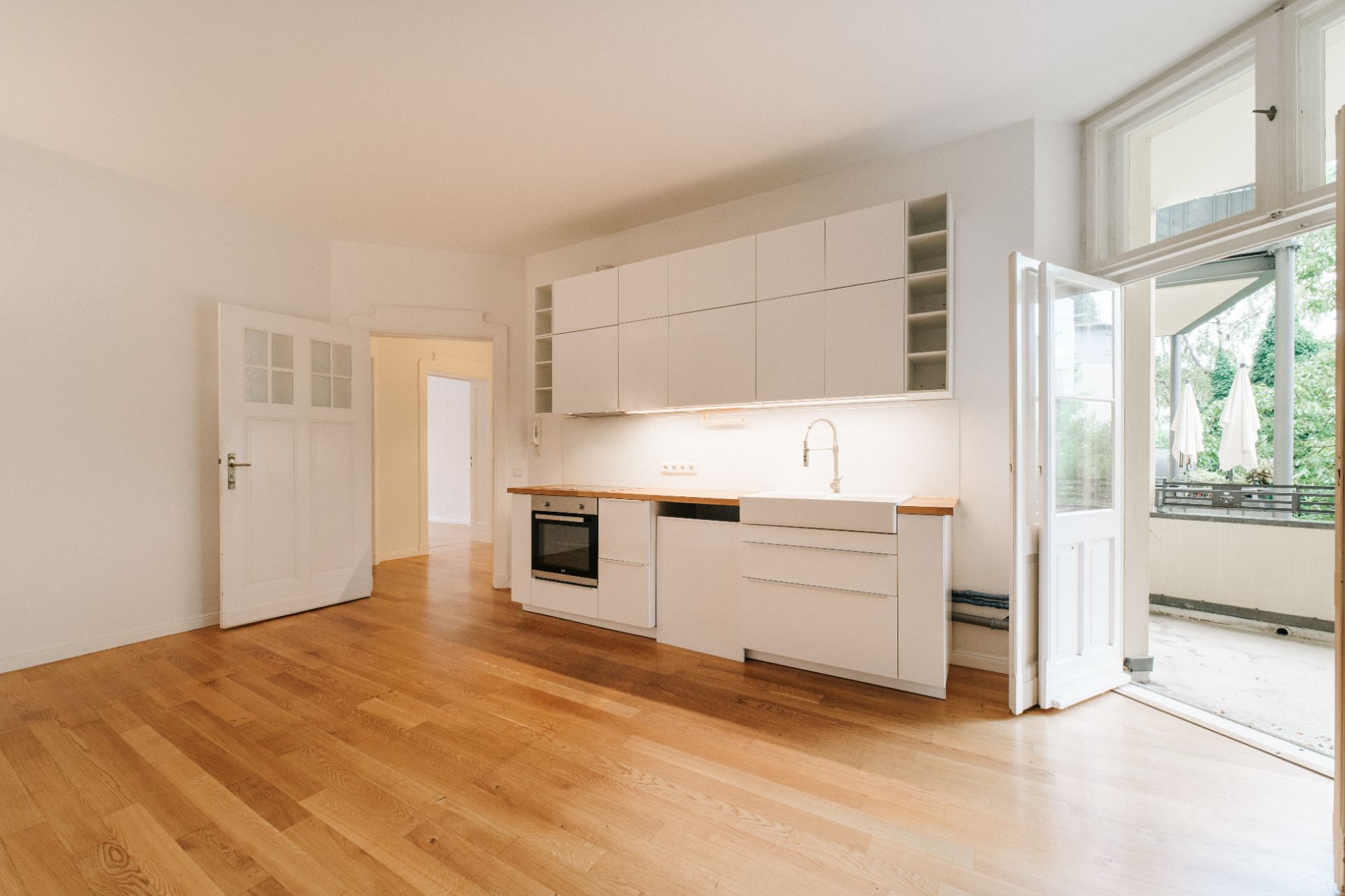 Helle Küche mit weißen Schränken, Holzfußboden und Zugang zu einem Balkon.
