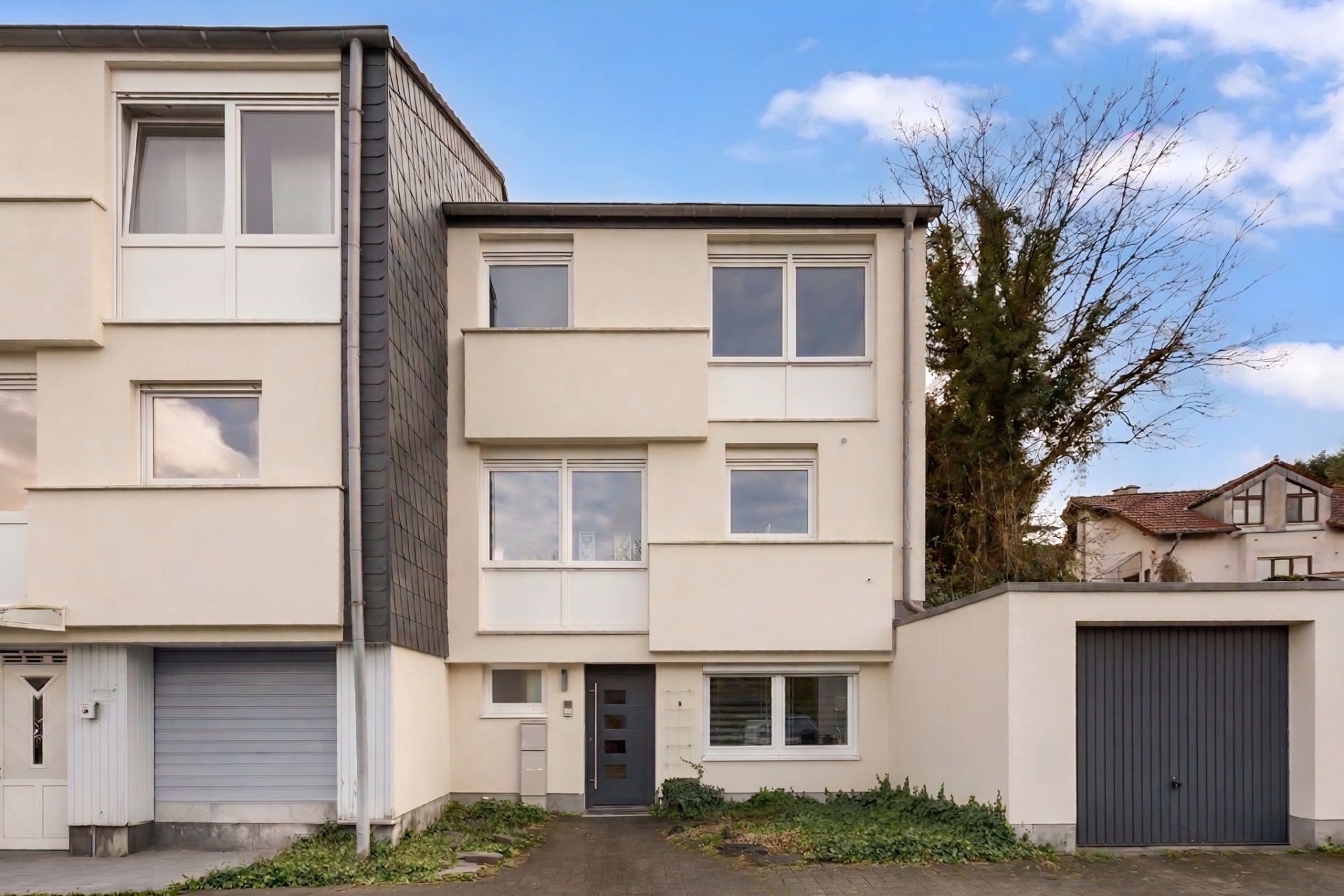 Modernes dreistöckiges Wohnhaus mit Garage und großen Fenstern, daneben ein weiteres Haus.