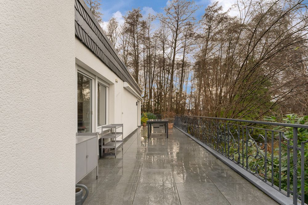 Große Terrasse mit Fliesenboden, Metallgeländer und Blick auf Bäume.