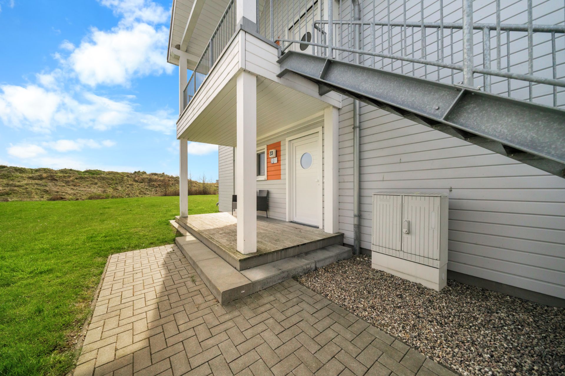 Eingang eines Wohnhauses mit Treppe, überdachter Veranda und gepflastertem Weg.