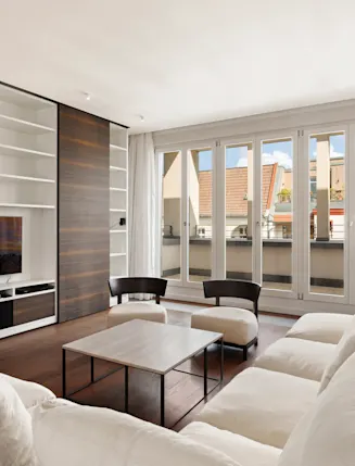 Helles Wohnzimmer mit weißem Sofa, Couchtisch, Regalwand und großen Fenstern zur Terrasse.