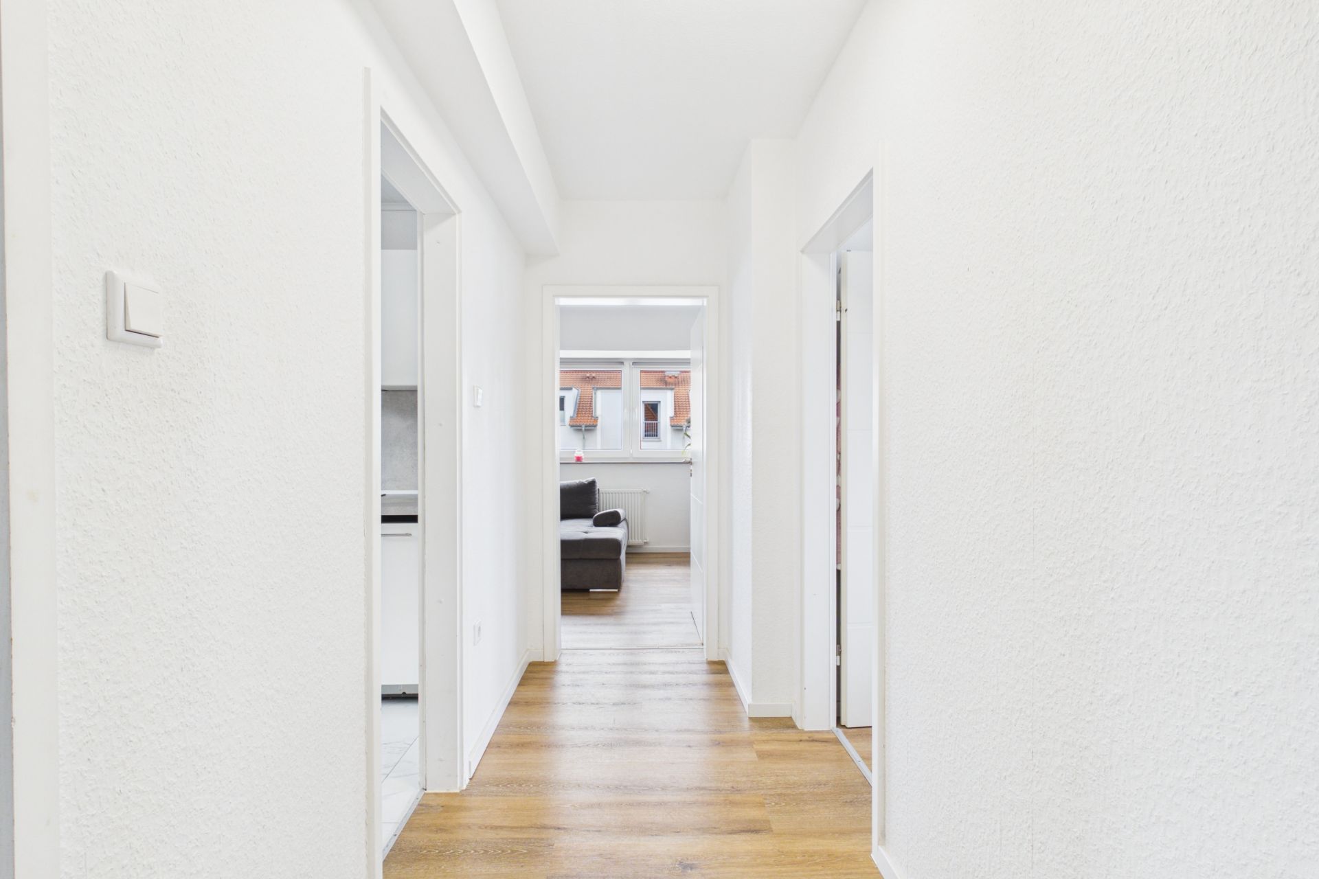 Heller Flur mit Holzboden, mehreren Türen und Blick auf ein Wohnzimmer mit Sofa.