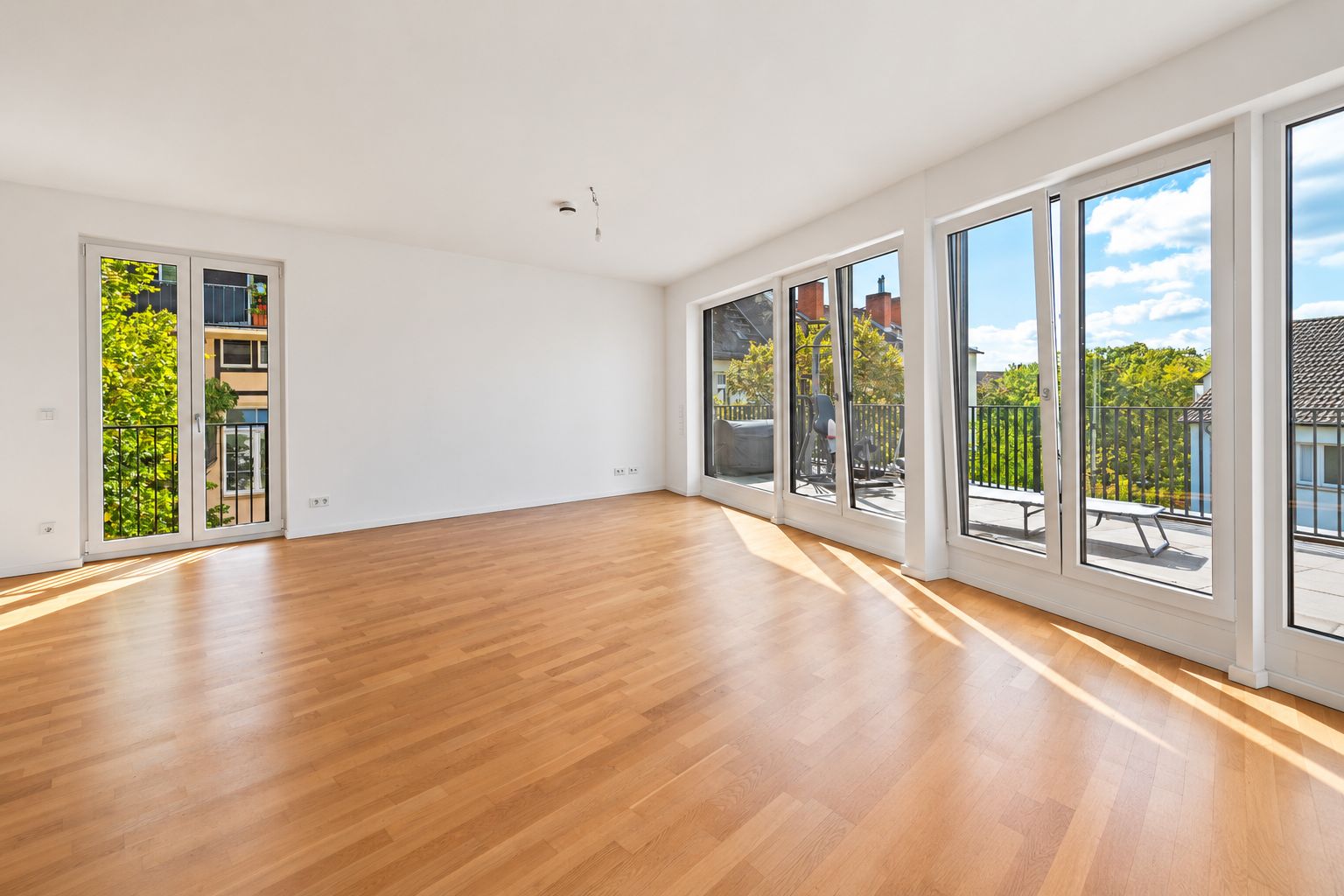 Helles Wohnzimmer mit Parkettboden und großen Fenstern zu einem Balkon.