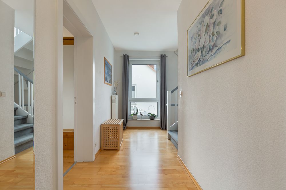 Heller Flur mit Holzboden, Treppe, großem Fenster und Wandbildern.