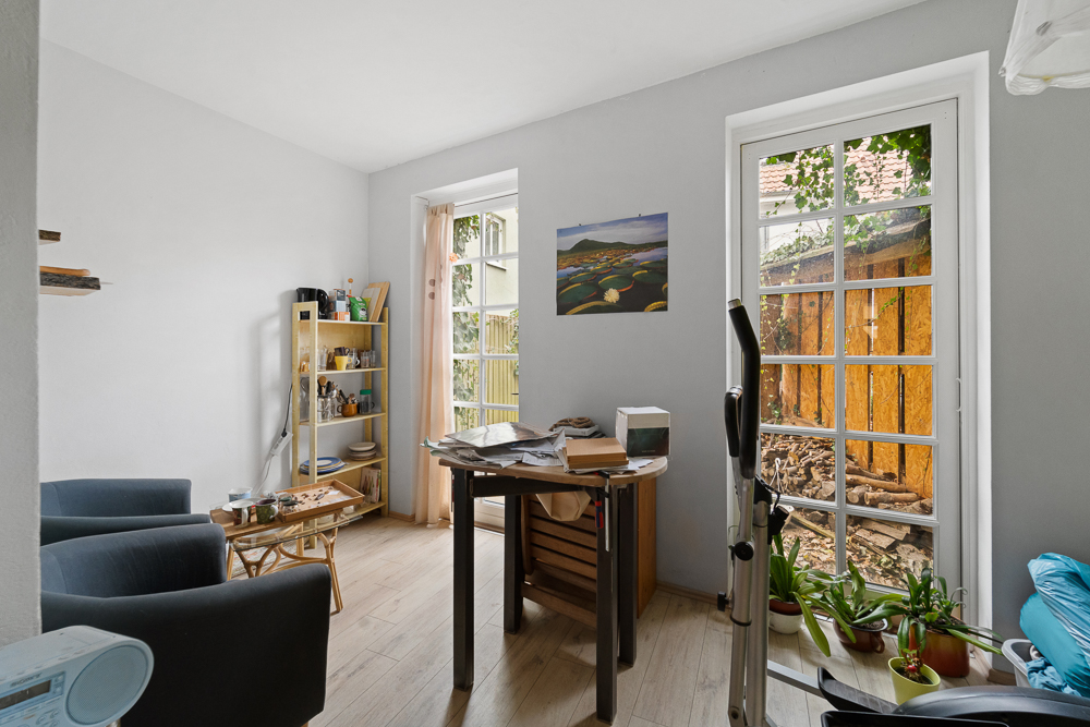 Wohnzimmer mit zwei Sesseln, Regal, Tisch, Pflanzen und Fenstertüren zum Garten.